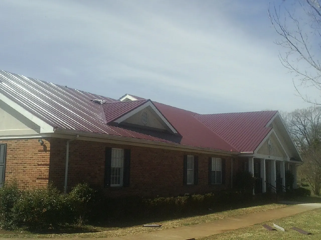 Red metal roof with gabled entries on a long brick building, from a Hail Damage Roof Repair job in Minier