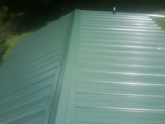 New green metal panels meeting at the ridge of a roof — Flat Roof Repair work by our crew in Minier