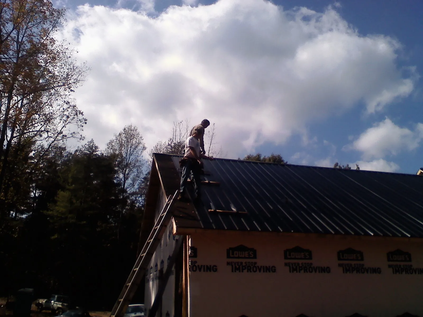 Roofer fastening dark metal panels high against a cloudy sky, from a Roof Inspection job in Minier