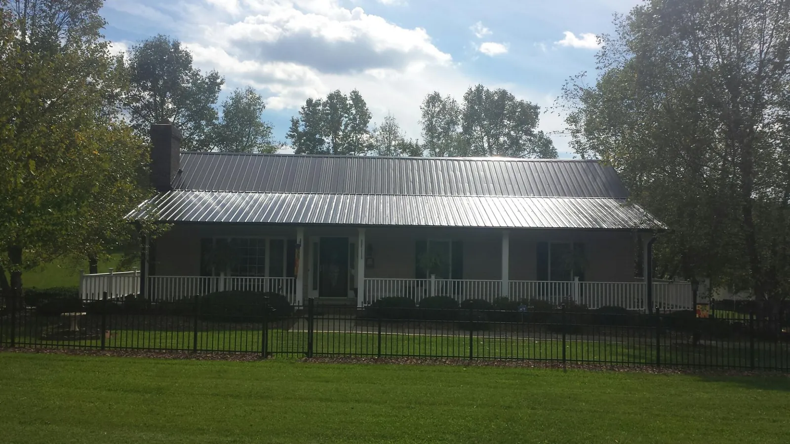 Gray metal roof on a brick ranch with a full width front porch — Gutter Guard Installation work by our crew in Minier