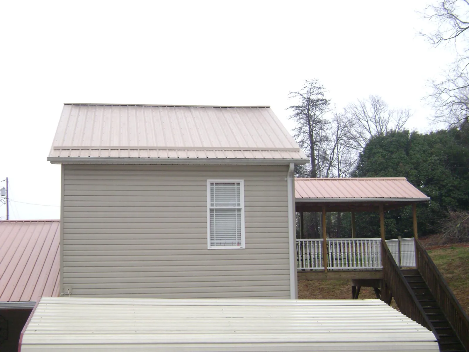 Tan metal roofs on a two story addition and attached porch, from a Roof Replacement job in Minier